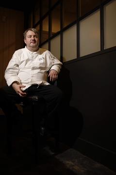 Chef relaxes in a contemporary restaurant setting, preparing to share culinary insights.
