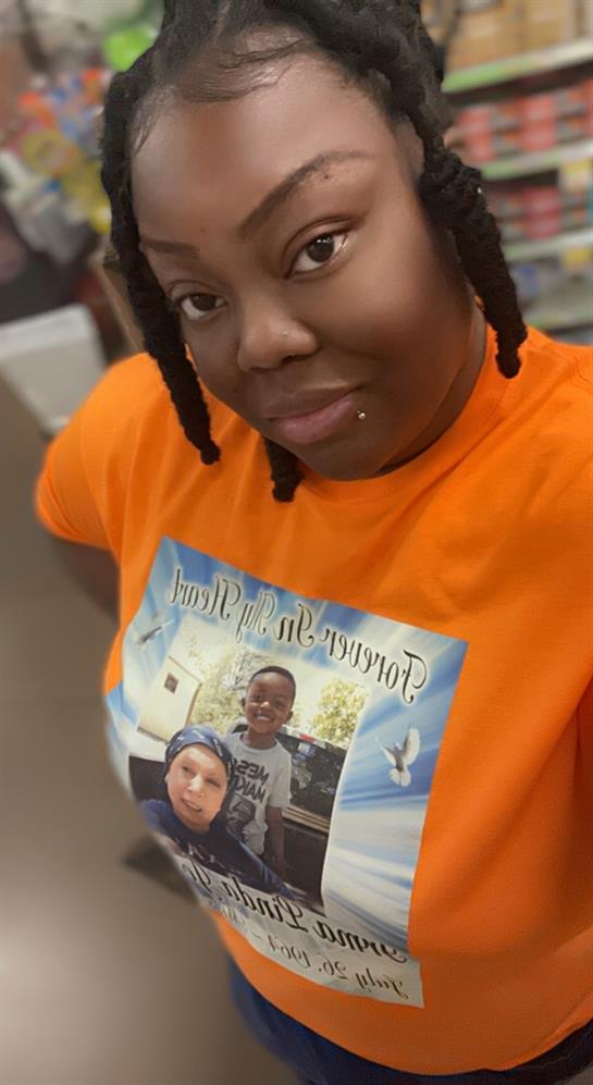 Individual smiles while showcasing an orange shirt featuring a cherished family photo.