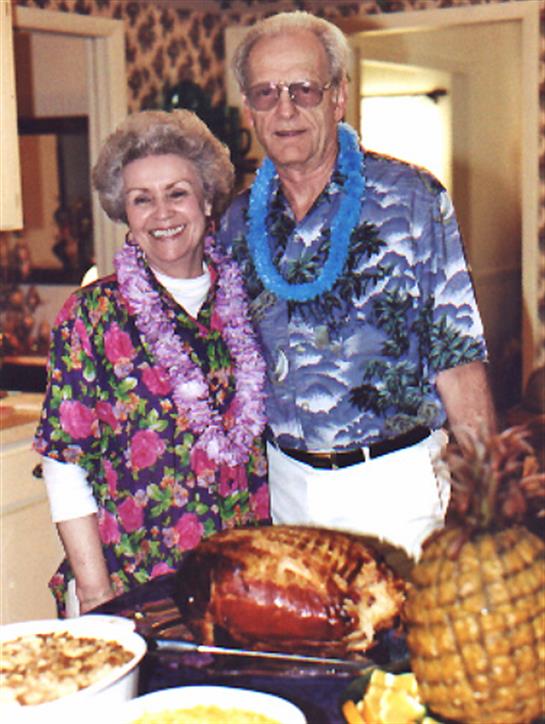 Joyful couple dressed in vibrant clothing stands by a decorated table with food.