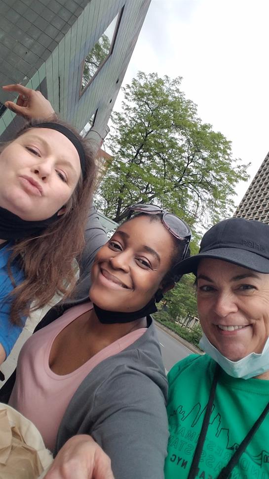 Three friends smile broadly and pose close together in a lively urban environment, showcasing joy.