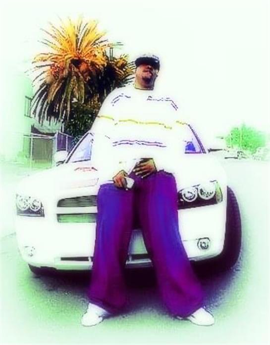 A man stands next to a white car in an urban setting with palm trees, showcasing a stylish outfit.