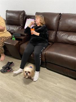 Group of individuals unwind on a couch, enjoying snacks and drinks, with a dog lying near them.