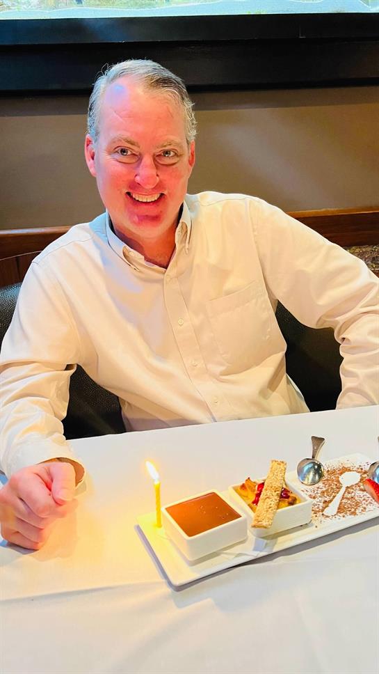 A man smiles happily while savoring dessert at a restaurant table during a special celebration.
