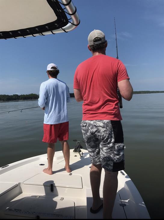 Two friends are fishing from a boat under a clear blue sky on a tranquil day.