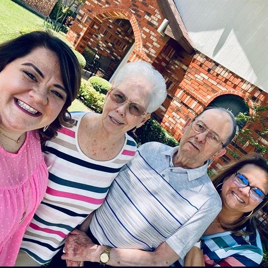 Four people stand together outside a brick house, smiling and enjoying their time together.