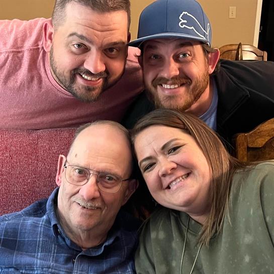 Four family members share smiles and laughter in a warm living room setting, celebrating together.