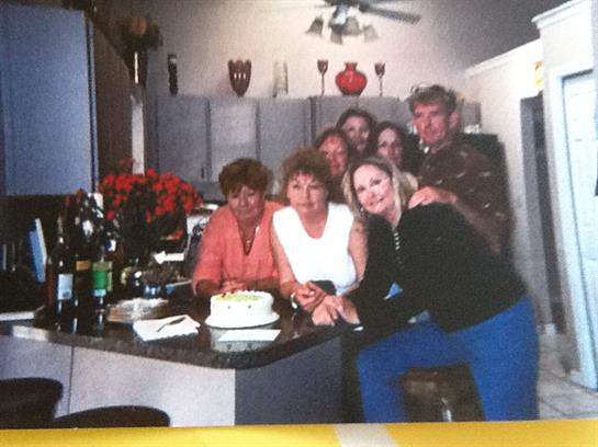A lively birthday celebration with friends gathered around a cake in a cozy home setting.