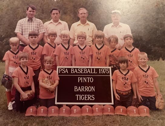 Young athletes stand in front of a sign, showcasing their team spirit in orange uniforms.