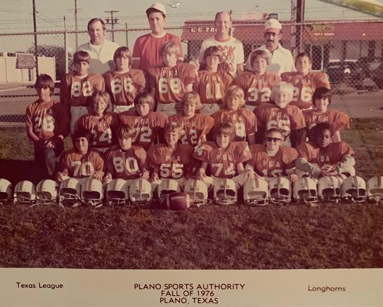 A group of young football players and coaches poses together in their uniforms on a sunny day.