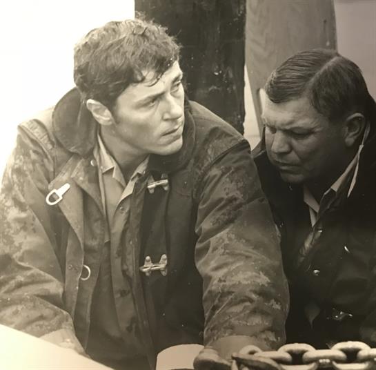 Two men are having an intense discussion on a ship's deck, surrounded by nautical surroundings.