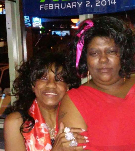 Two women pose happily, showcasing their colorful outfits and joyful expressions at night.