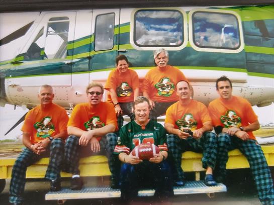 Friends gather outside a helicopter, wearing colorful shirts and enjoying a playful moment together.