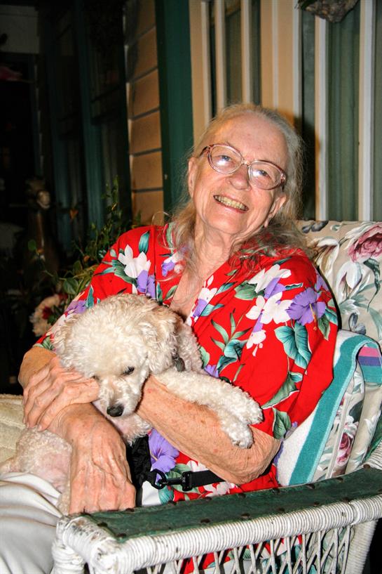 Elderly woman happily holds a small fluffy dog while sitting on a vibrant floral couch.