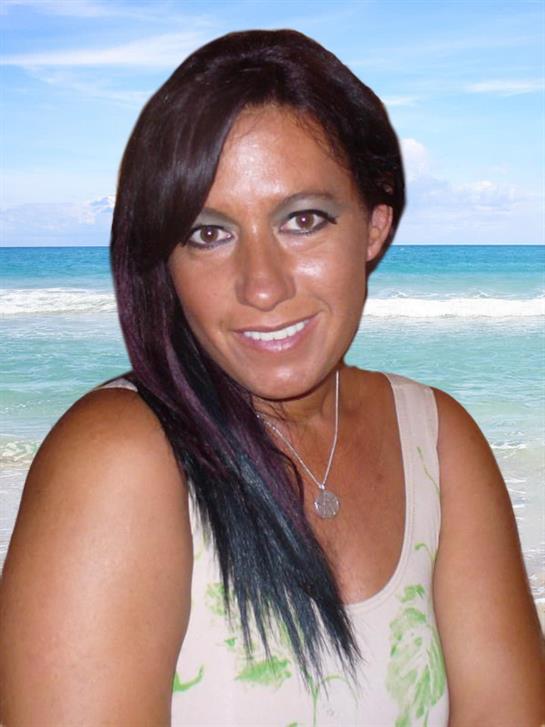 A woman with long dark hair enjoys a sunny day at the beach, smiling happily by the ocean.
