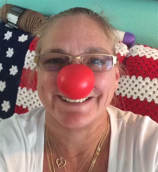 A woman shows off her playful side with a bright red clown nose, smiling in a colorful room.