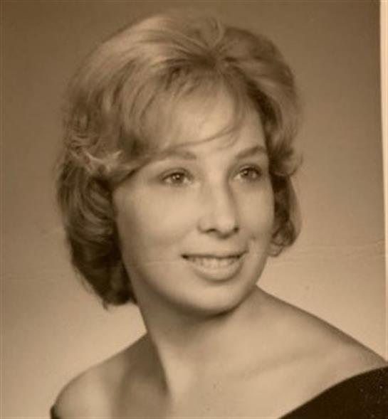 A young woman smiles gracefully, showcasing her styled hair and classic attire typical of the 1960s.