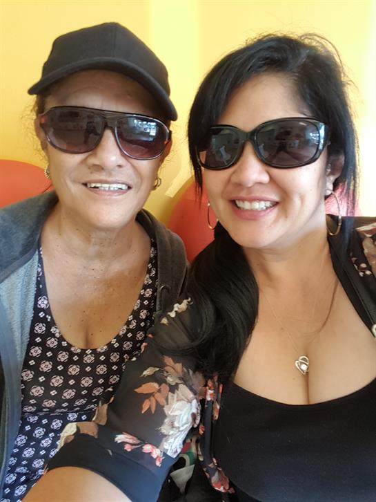 Two women are smiling while sitting in a colorful indoor space wearing sunglasses.