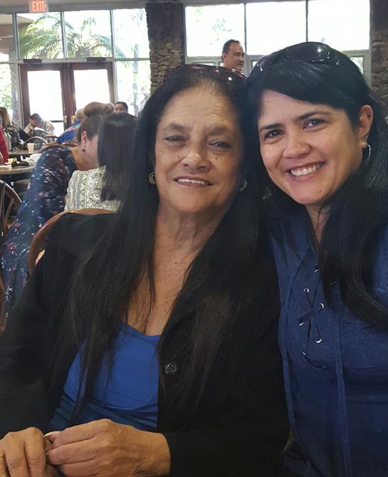 Two women sit closely together, smiling joyfully while enjoying a family dining experience.