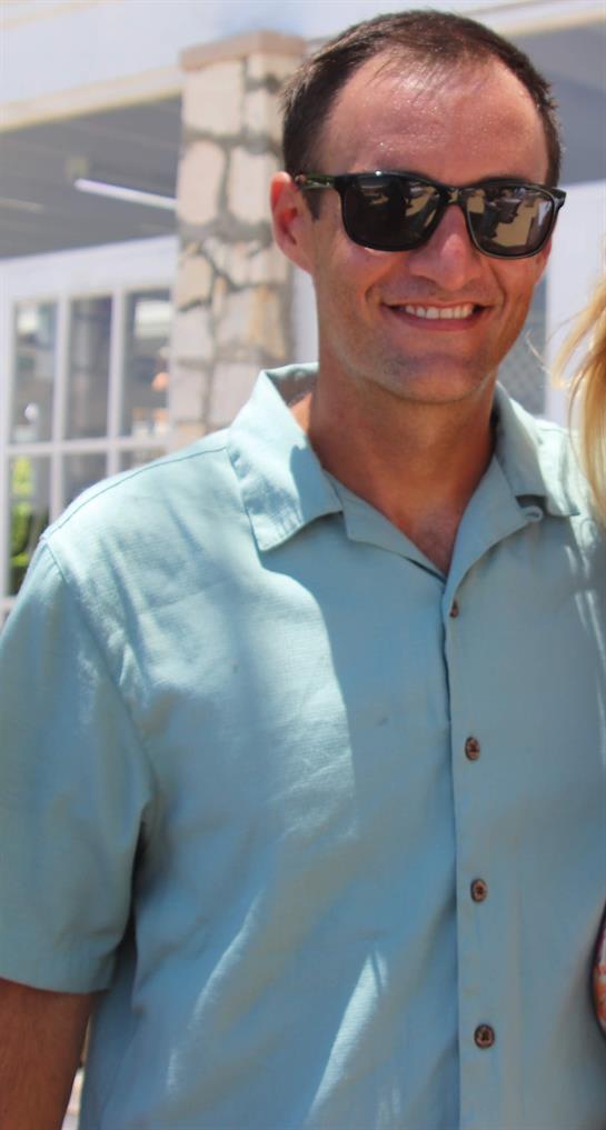 Two people share a joyful moment outdoors, smiling at the camera by a well-lit structure.