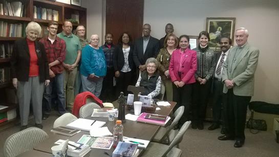 Diverse group of individuals participating in a community meeting around a table.