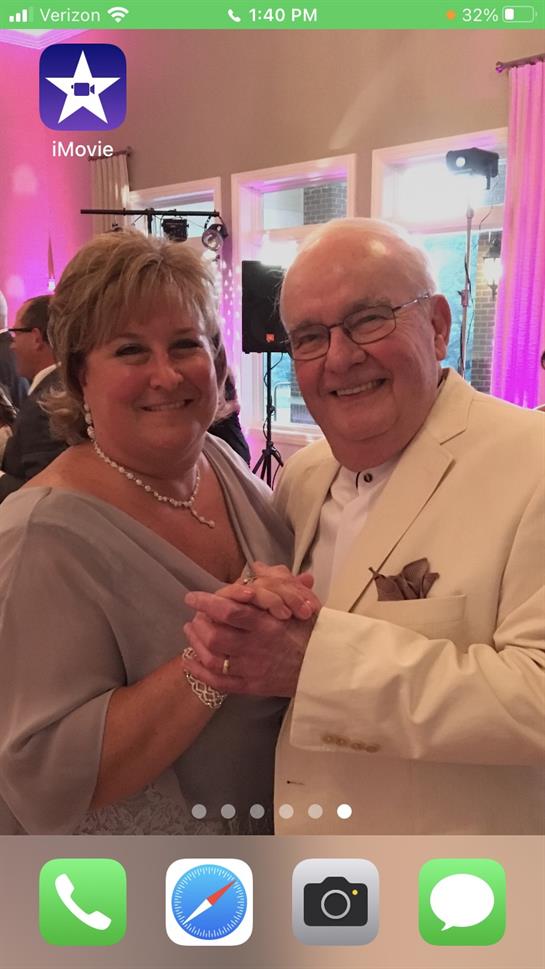 An elderly couple enjoys dancing together at a wedding reception with vibrant lights.
