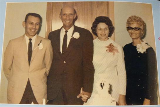 Four well-dressed people stand together, celebrating a joyous occasion in a cozy indoor location.