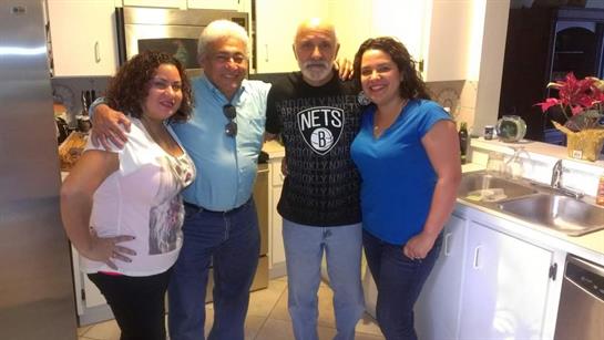Four family members smile together in a warm kitchen, enjoying quality time during a sunny day.