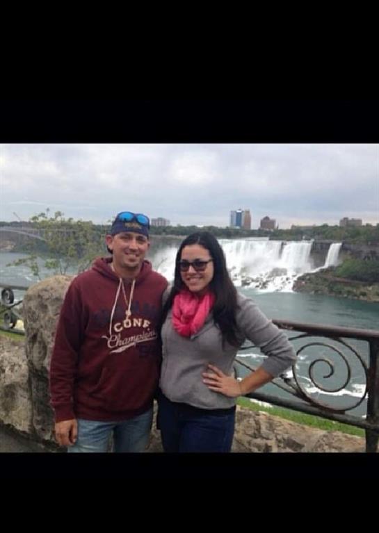 A couple joyfully poses at Niagara Falls, with the stunning waterfall behind them.