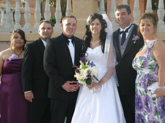 A joyful couple stands with family and friends during their wedding ceremony in a bright location.