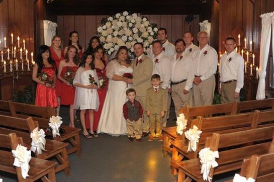 A couple stands at the altar surrounded by family and friends in a festive indoor wedding setting.