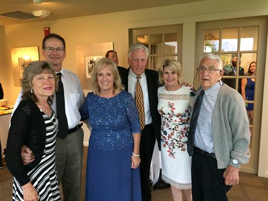 Six friends joyfully pose together, dressed smartly for a celebration in a cozy venue.