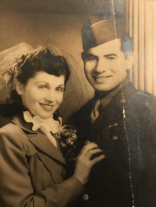 A smiling couple dressed in vintage clothing stands close together, exuding warmth and affection.