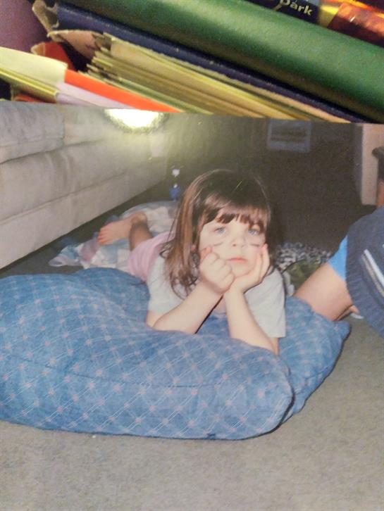 A child lays on a blue cushion while others lounge nearby in a comfortable living room.