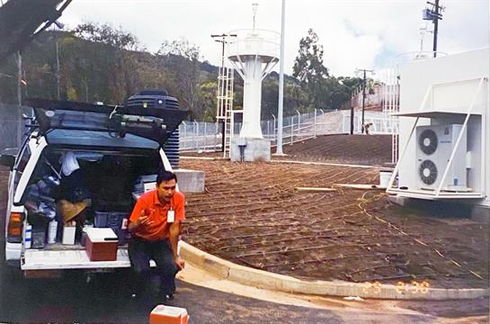 A delivery worker is unloading packages from a vehicle near a water tower in a rural setting.