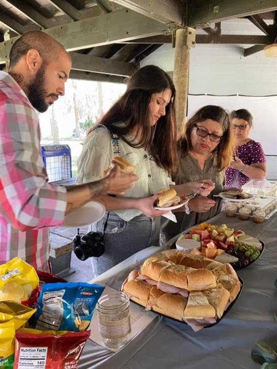 Friends gather around a table filled with various foods, sharing and enjoying each other's company.