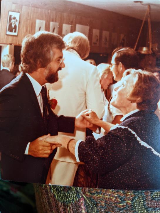 A man and woman engage in a spirited dance surrounded by other guests enjoying the party atmosphere.