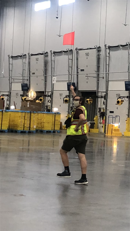 A joyful worker in a reflective vest dances playfully in a spacious warehouse during break time.