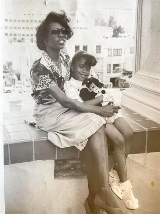 A mother sits on a bench with her daughter, who holds a stuffed animal.