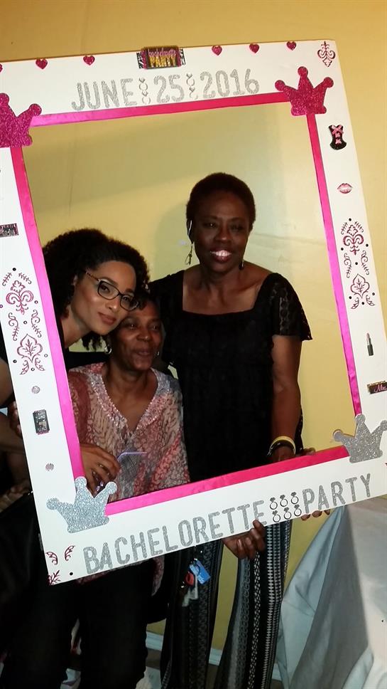 Three women joyfully pose together with a decorative frame during a festive celebration.