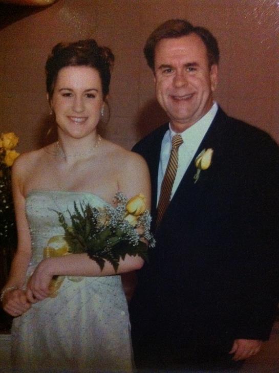 Bride and father smile together, surrounded by flowers, during a joyful celebration moment.