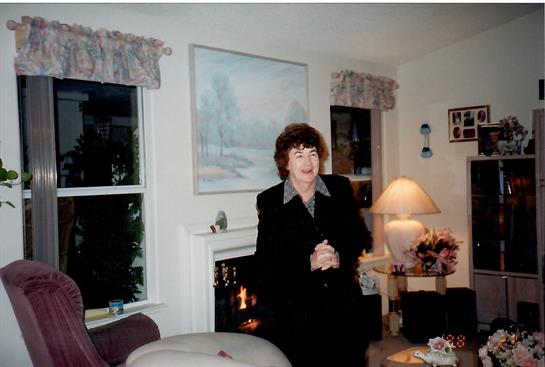 A woman in formal attire stands gracefully in a warmly lit living room with decorative features.