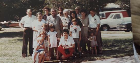Large group of family members posing joyfully outdoors in a park on a sunny day.