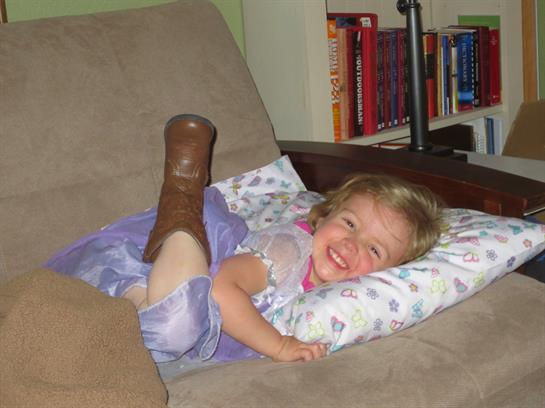 Young child in a dress lies on a couch, laughing and relaxed with a playful pose.