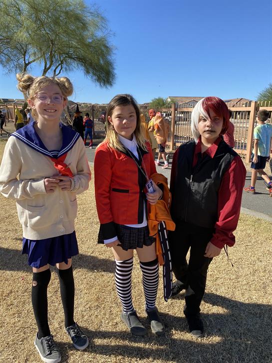 Three children wear colorful costumes and pose together during a lively outdoor celebration.