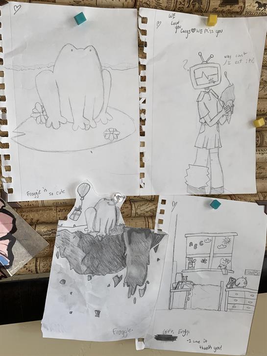 Various drawings created by children hang on a wall, featuring whimsical characters and scenes.