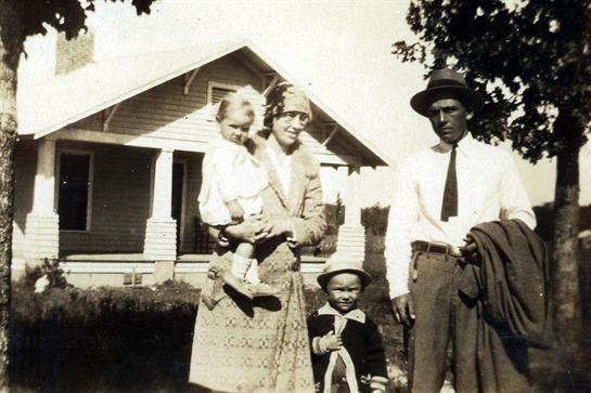 Family poses together on a sunny day in front of an old home, capturing a moment in history.