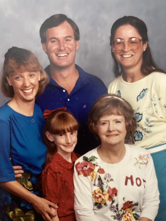 A group of five people smiles joyfully while standing closely together indoors, showing warmth.