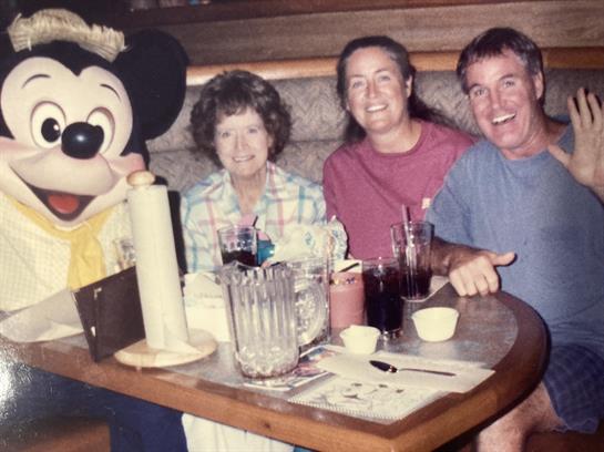 Friends gather around a large character in a fun dining atmosphere, smiling and celebrating.