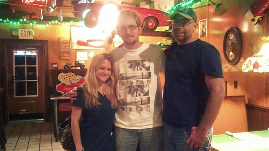 Three friends pose together in a vibrant diner featuring nostalgic decor and bright lights.