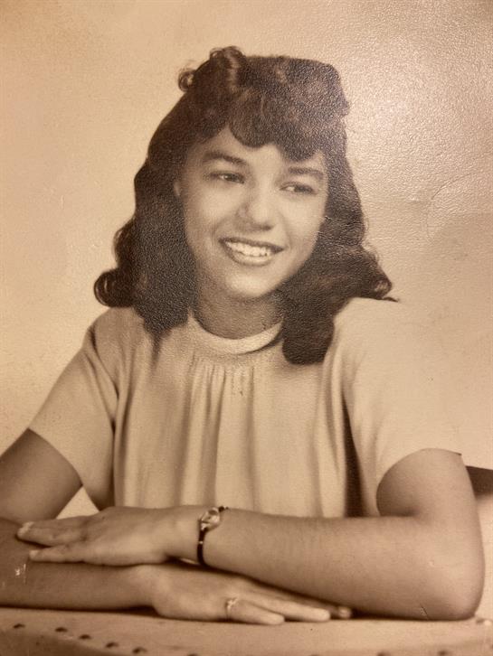 Young woman with curly hair smiles brightly while seated, expressing confidence and warmth.